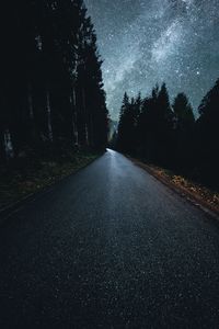 Empty road amidst trees in forest against sky at night