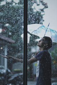 Man holding umbrella in rain seen through window