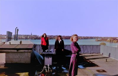 Portrait of smiling female friends standing by lake against clear sky during sunny day