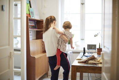 Female influencer carrying daughter while standing by table at home