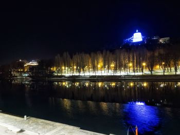 Illuminated city by sea against sky at night