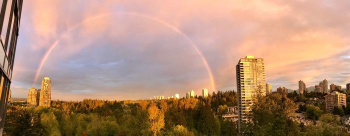 Panoramic view of rainbow over city against cloudy sky