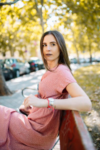 Thoughtful young woman using phone while sitting on bench