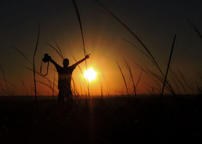 Silhouette man standing on field against sky during sunset