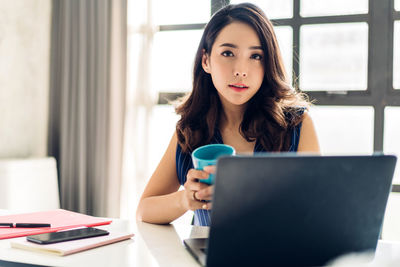 Portrait of young woman using mobile phone while sitting on table