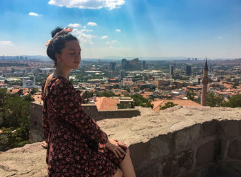 Young woman looking at city buildings against sky at viewpoint