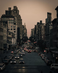 Cars on city street by buildings against sky during sunset