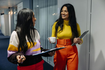 Happy female entrepreneurs discussing with each other while walking in corridor at office