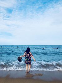 Rear view of woman standing at beach against sky