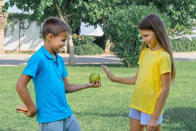 Teenage boy and girl with apple and burger in the park. choice between healthy and unhealthy food.