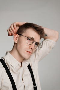 Close-up of young man wearing eyeglasses looking away against white background