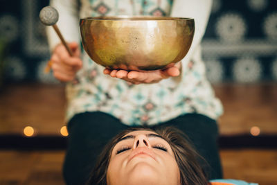 Midsection of therapist playing rin gong by young woman at spa