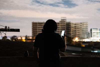 Rear view of silhouette man standing against sky in city