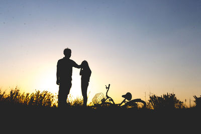 Silhouette man consoling girl on field against clear sky during sunset