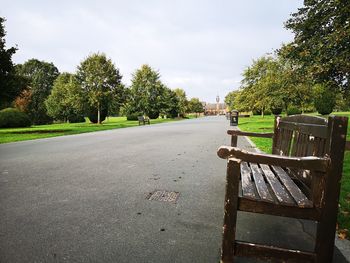 Empty park bench by road against sky