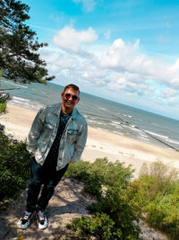 Young man standing on beach against sky