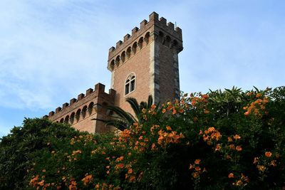 Tower of the castle of bolgheri with orange flowers and blue sky in tuscany