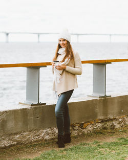 Portrait of young woman holding coffee while standing outdoors during winter