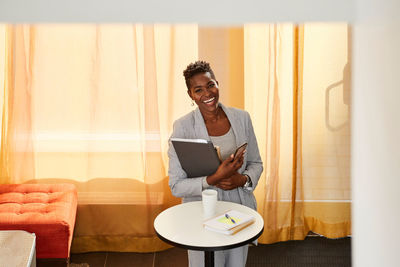 Portrait of smiling businesswoman with smart phone and files standing in office