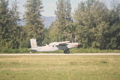 Side view of airplane on field against trees