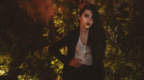 Portrait of beautiful young woman posing against trees at night