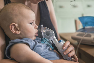 Midsection of mother assisting son in breathing with oxygen mask at home