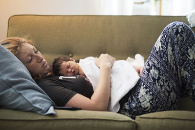 Side view of woman sleeping with baby boy on sofa at home