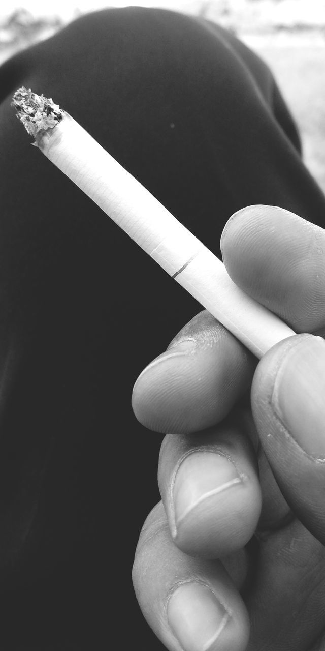 CLOSE-UP OF HUMAN HAND HOLDING CIGARETTE ON GROUND