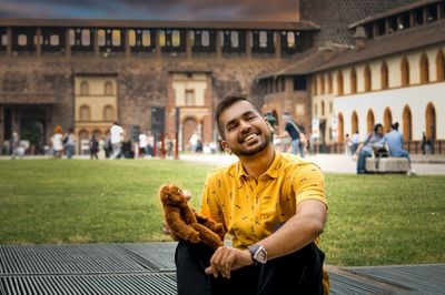 Portrait of cheerful young man holding toy animal while sitting against building