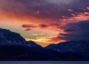 Scenic view of lake against dramatic sky during sunset