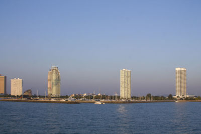 Sea by modern buildings against clear sky