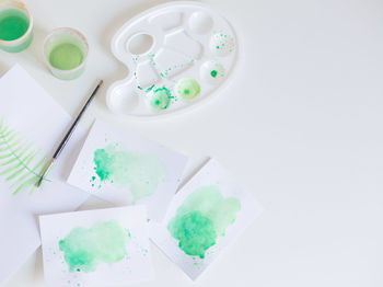 High angle view of palette with papers and paintbrush on white background