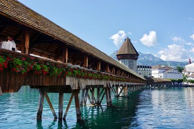 Bridge over river by houses and buildings against sky