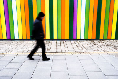 Full length of man walking on footpath against wall