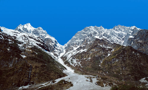 Low angle view of snowcapped mountains against clear blue sky