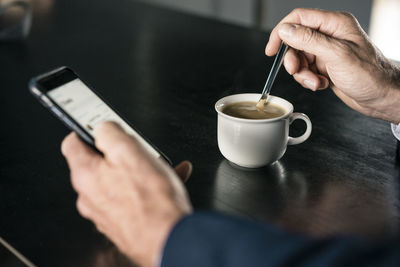 Close-up of businessman with cup of coffee using cell phone