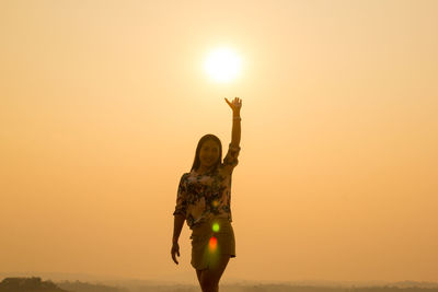 Portrait of woman gesturing while standing against sky during sunset