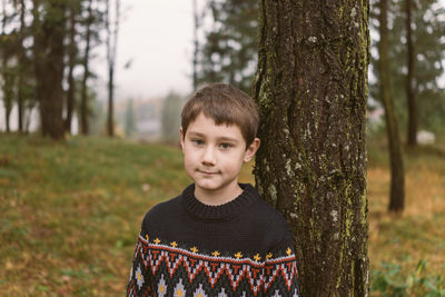Portrait of cute boy standing by tree at forest