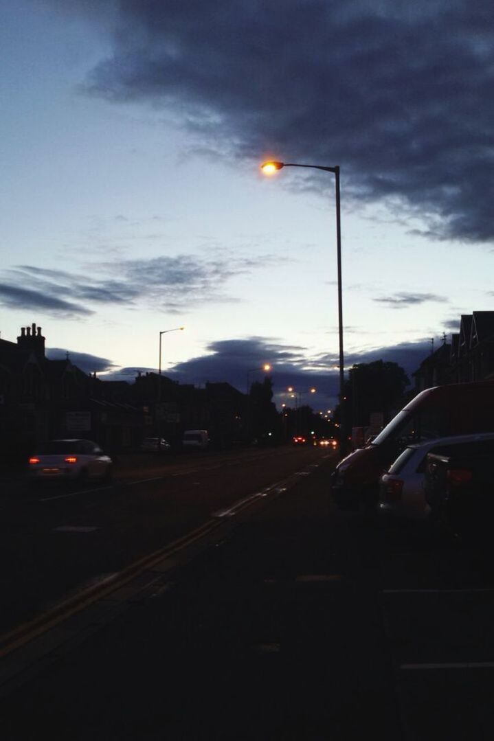 transportation, car, street light, sky, land vehicle, mode of transport, road, street, cloud - sky, illuminated, the way forward, city, road marking, building exterior, sunset, lighting equipment, dusk, cloudy, on the move, silhouette