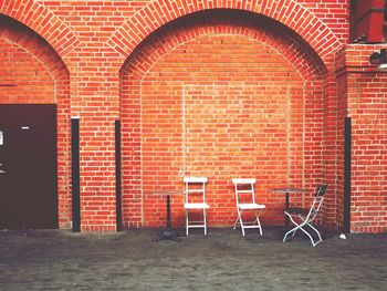 Chairs and table on sidewalk against brick wall