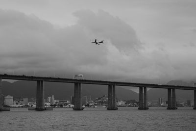 Airplane flying over bridge against sky
