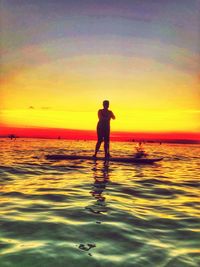 Silhouette man standing in sea against sky during sunset