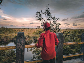 Rear view of man standing by railing against sky