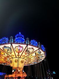 Illuminated ferris wheel against clear blue sky at night
