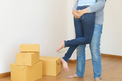 Midsection of couple embracing by cardboard boxes on hardwood floor at home