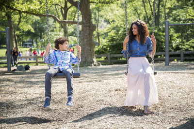 Mother and son looking at each other while playing swing in park