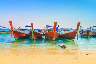 Boats moored on beach against clear blue sky