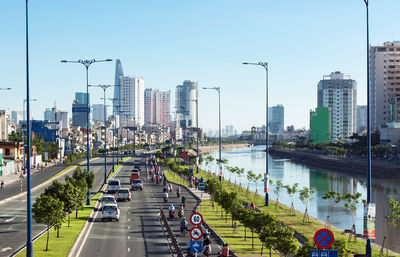 Vehicles on road by river against buildings in city