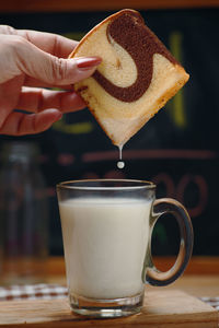 The woman's hand dip the marble cake into the milk in a glass of milk