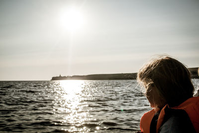 Rear view of woman by sea against sky on sunny day
